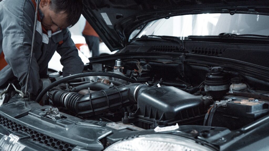 A mechanic in a grey uniform inspecting the engine of a car
