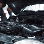 A mechanic in a grey uniform inspecting the engine of a car